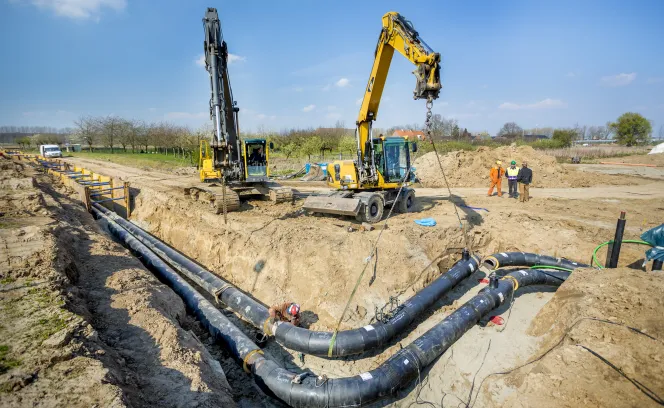 Leidingen worden door twee graafmachines in de grond gelegd